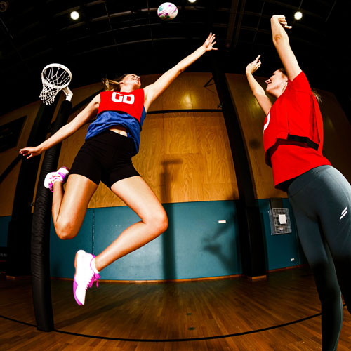 Netballer, Maddy Turner defending shooter on court. Netball players shooting for goal on court in netball game. Netballers are wearing netball bibs.
